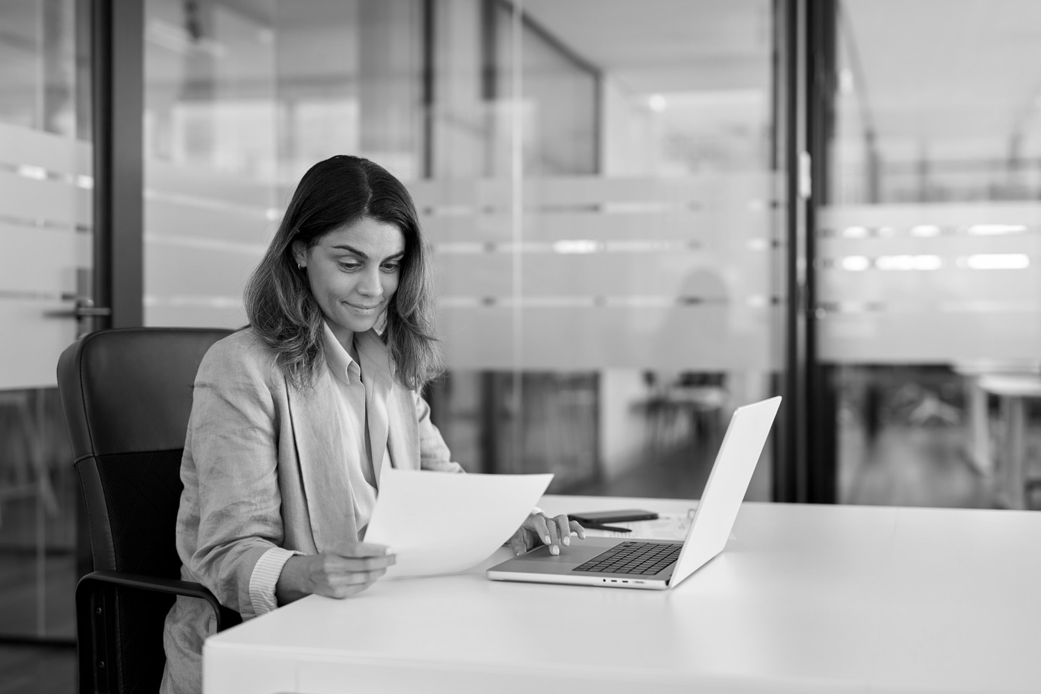 Business professional reviewing documents at her desk with a laptop.